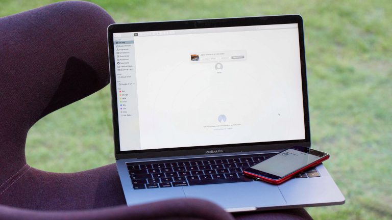 Ein MacBook steht auf einem Sessel. Auf der Tastatur des Laptops liegt ein iPhone SE.