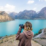 Eine Person steht vor einer Berglandschaft mit See und fotografiert.
