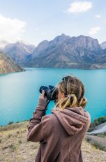 Eine Person steht vor einer Berglandschaft mit See und fotografiert.