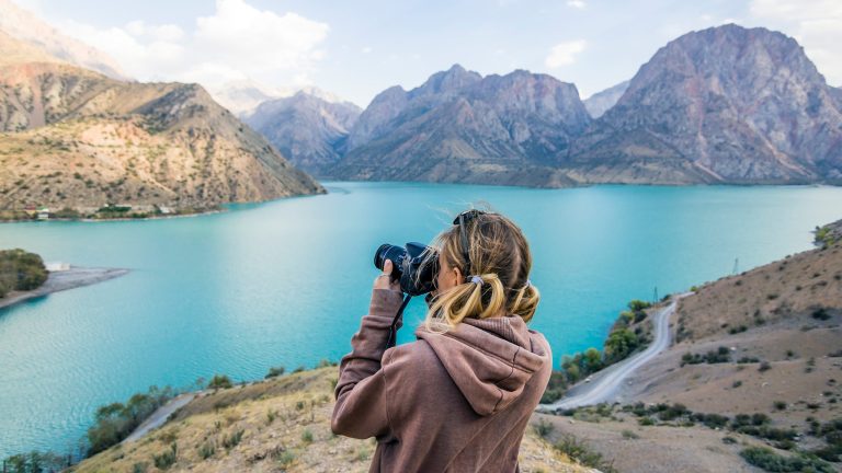 Eine Person steht vor einer Berglandschaft mit See und fotografiert.