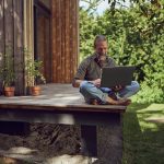 Eine Person sitzt mit einem Laptop auf einer Terrasse.