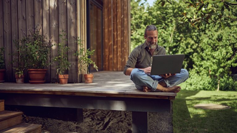 Eine Person sitzt mit einem Laptop auf einer Terrasse.