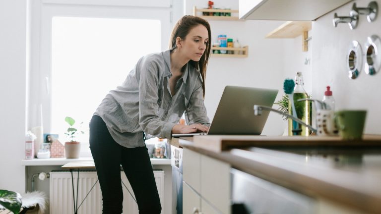 Eine Person steht in einer Küche mit einem Laptop auf der Arbeitsfläche.