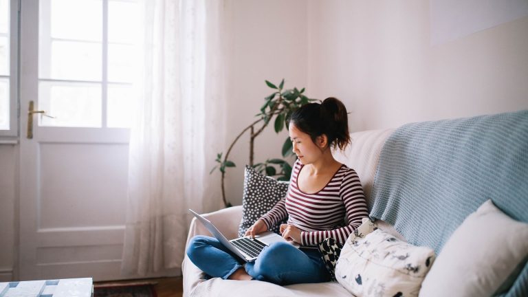 Eine Person sitzt auf einem Sofa und schaut auf einen Laptop.