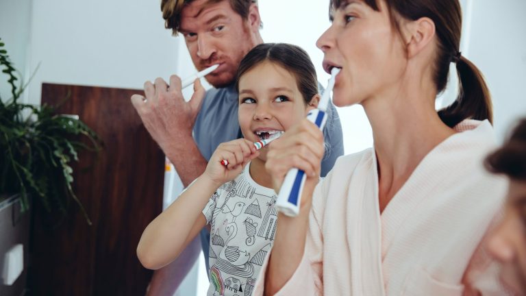 Eine Familie steht im Bad und putzt sich mit elektrischen Zahnbürsten die Zähne.