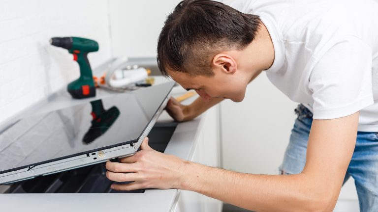 Eine Person fasst ein Induktionskochfeld in eine Arbeitsplatte ein Im Hintergrund ist etwas Werkzeug zu sehen.