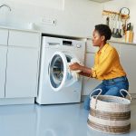 Eine Person gibt Wäsche in eine Waschmaschine, die in eine Küchenzeile eingebaut ist.