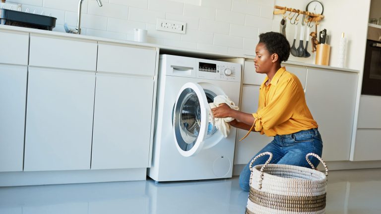 Eine Person gibt Wäsche in eine Waschmaschine, die in eine Küchenzeile eingebaut ist.