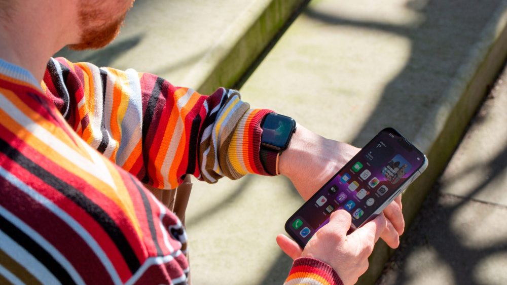 Eine Person trägt eine Apple Watch am Handgelenk und hält in der rechten Hand ein iPhone.