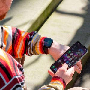 Eine Person trägt eine Apple Watch am Handgelenk und hält in der rechten Hand ein iPhone.