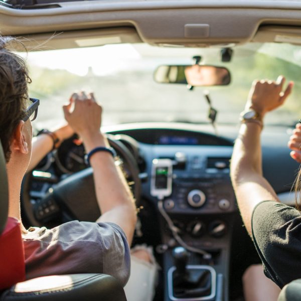 Zwei Personen sitzen in einem Auto und scheinen sich zu Musik zu bewegen. An der Mittelkonsole ist ein Smartphone angesteckt.