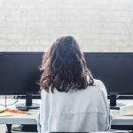 Eine Person sitzt vor zwei Bildschirmen, auf denen nichts zu sehen ist.