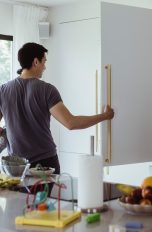 Einbaukühlschrank ausbauen Eine Person mit einem Kind auf dem Arm öffnet den Einbaukühlschrank in einer weißen Küche.