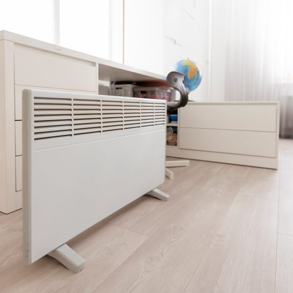 Eine Elektroheizung steht vor einem Schreibtisch am Boden.