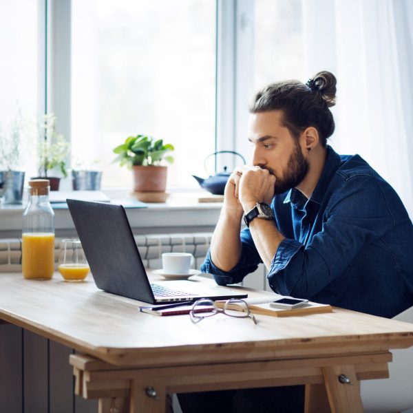 Eine Person sitzt vor einem Laptop und st&uuml;tzt den Kopf auf die F&auml;uste.
