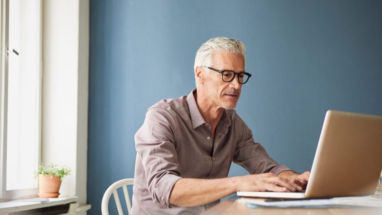 Eine Person sitz an einem Tisch und arbeitet an einem Laptop.