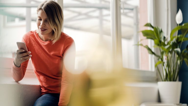 Eine Person blickt auf ihr Smartphone, das sie in der rechten Hand hält.