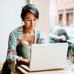 Eine Person sitzt in einem Caf&eacute; und bedient einen Laptop.