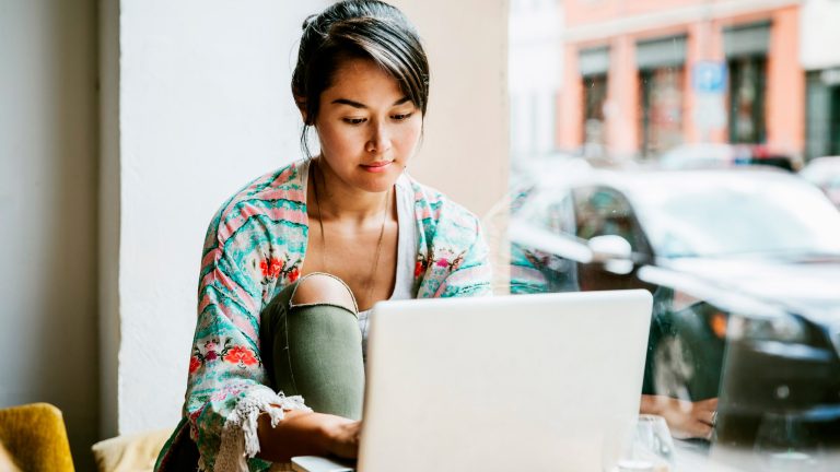 Eine Person sitzt in einem Café und bedient einen Laptop.