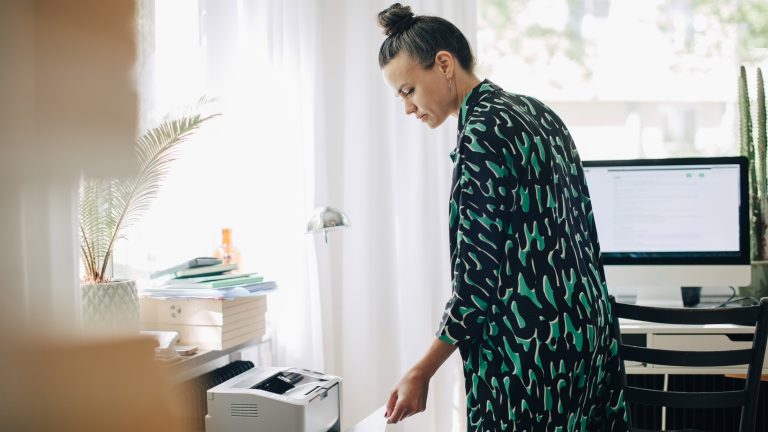 Eine Person steht vor einem Drucker und nimmt ein Blatt Papier aus der Ausgabe.