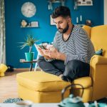Eine Person sitzt in einem gelben Ohrensessel und bedient ein Smartphone.