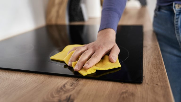 Eine Person reinigt ein Cerankochfeld mit einem gelben Schwammtuch.