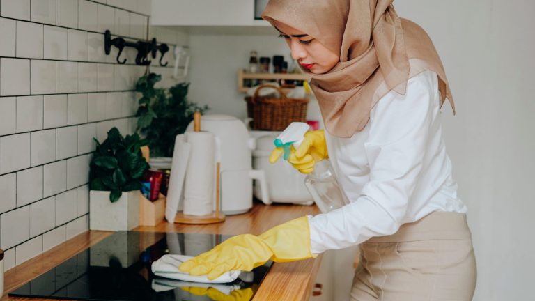 Eine Person reinigt ein Ceranfeld mit Glasreiniger und einem Tuch.