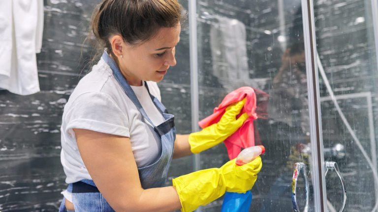 Eine Person reinigt eine Duschkabine aus Glas.