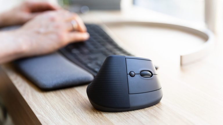 Eine Logitech Lift im Fokus. Die vertikale Maus steht neben einer Tastatur, auf der eine Person tippt.