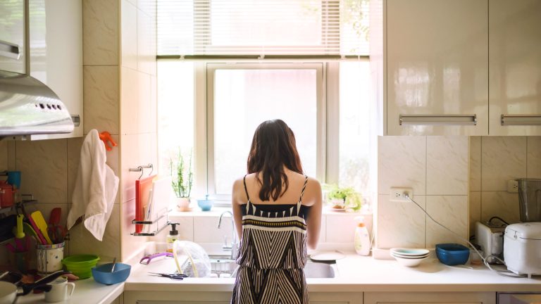 Eine Person ist von hinten zu sehen, wie sie vor einem Spülbecken steht und Geschirr abwäscht.