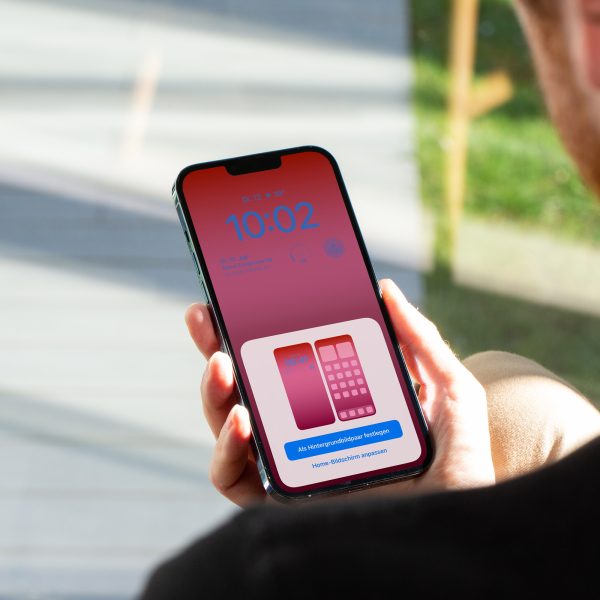 Eine Person h&auml;lt ein iPhone in der Hand, auf dem gerade die Einstellungsoptionen des Sperrbildschirms zu sehen sind.