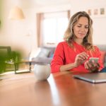 Eine Person sitzt an einem Tisch und bedient ein Smartphone.