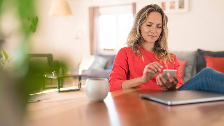 Eine Person sitzt an einem Tisch und bedient ein Smartphone.