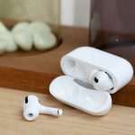 Ein Paar AirPods Pro liegt samt Ladecase auf einem Holzbrett. Einer der beiden Kopfh&ouml;rer liegt dabei vor der ge&ouml;ffneten H&uuml;lle.