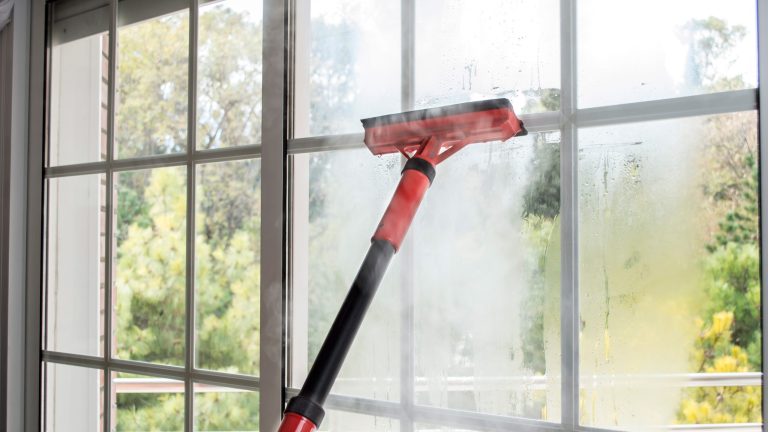Mit einem roten Dampfreiniger wird eine gro&szlig;e Fensterfront gereinigt.