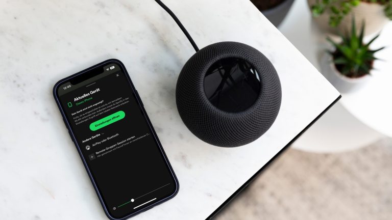 Ein schwarzer HomePod steht auf einem Tisch. Daneben liegt ein Smartphone, auf dem die Spotify-App geöffnet wurde.