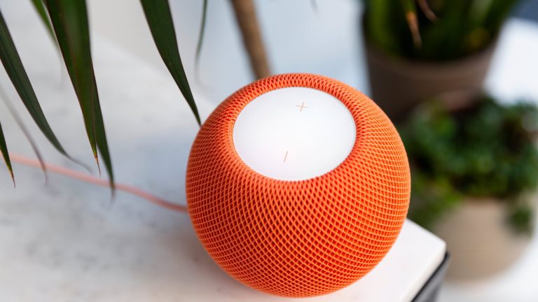 Ein HomePod mini in Orange steht auf einem Tisch mit einer Marmor-Platte.