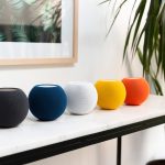 Auf einem Tisch stehen f&uuml;nf HomePod mini in den Farben Schwarz, Blau, Wei&szlig;, Gelb und Orange.