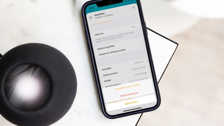 Ein schwarzer HomePod mini und ein iPhone 12 liegen auf einem Marmortisch.