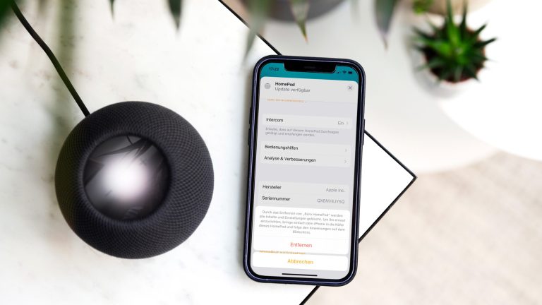 Ein schwarzer HomePod mini und ein iPhone 12 liegen auf einem Marmortisch.