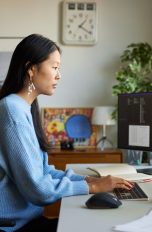 Eine Person sitzt vor zwei Monitoren auf einem Schreibtisch und tippt auf einer flachen Office-Tastatur.
