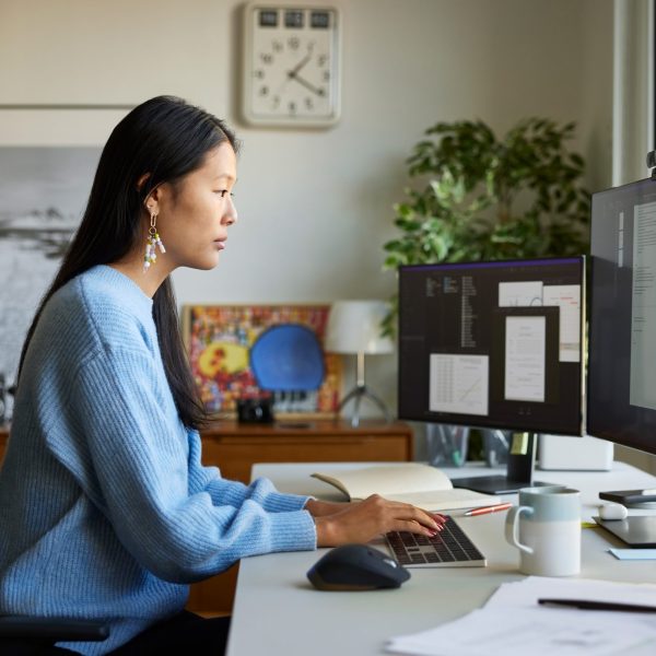 Eine Person sitzt vor zwei Monitoren auf einem Schreibtisch und tippt auf einer flachen Office-Tastatur.
