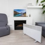 Eine Infrarotheizung steht in einem Wohnzimmer. Im Hintergrund ist ein Karmin zu sehen, auf dem ein Bild steht.