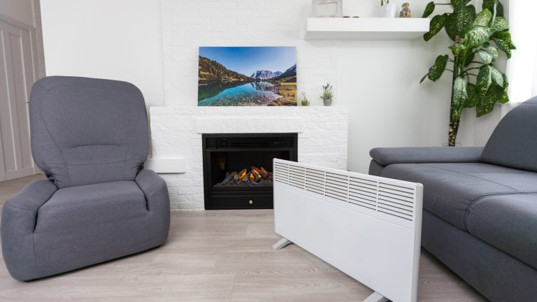 Eine Infrarotheizung steht in einem Wohnzimmer. Im Hintergrund ist ein Karmin zu sehen, auf dem ein Bild steht.
