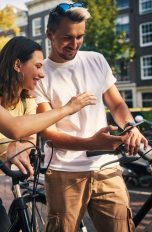Google Maps Routenplaner Zwei Personen auf Fahrrädern machen eine kurze Pause und schauen gemeinsam auf ein Smartphone.
