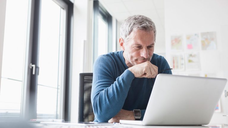 Eine Person lehnt sich leicht über einen Schreibtisch, um in den Bildschirm eines Laptops zu schauen.