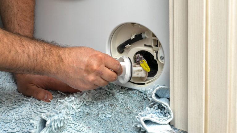 Eine Person entnimmt das Flusensieb einer Waschmaschine.