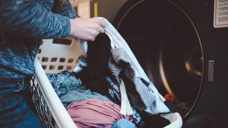 Eine Person steht mit einem Korb voll Wäsche vor einem Trockner.