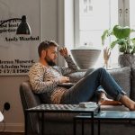 Eine Person sitzt mit einem Laptop auf den Knien auf einem Sofa.