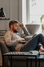 Eine Person sitzt mit einem Laptop auf den Knien auf einem Sofa. Eine Person sitzt mit einem Laptop auf den Knien auf einem Sofa.